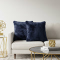 Two plush navy blue throw pillows displayed on a light beige sofa in a modern living room setting with gold accents.