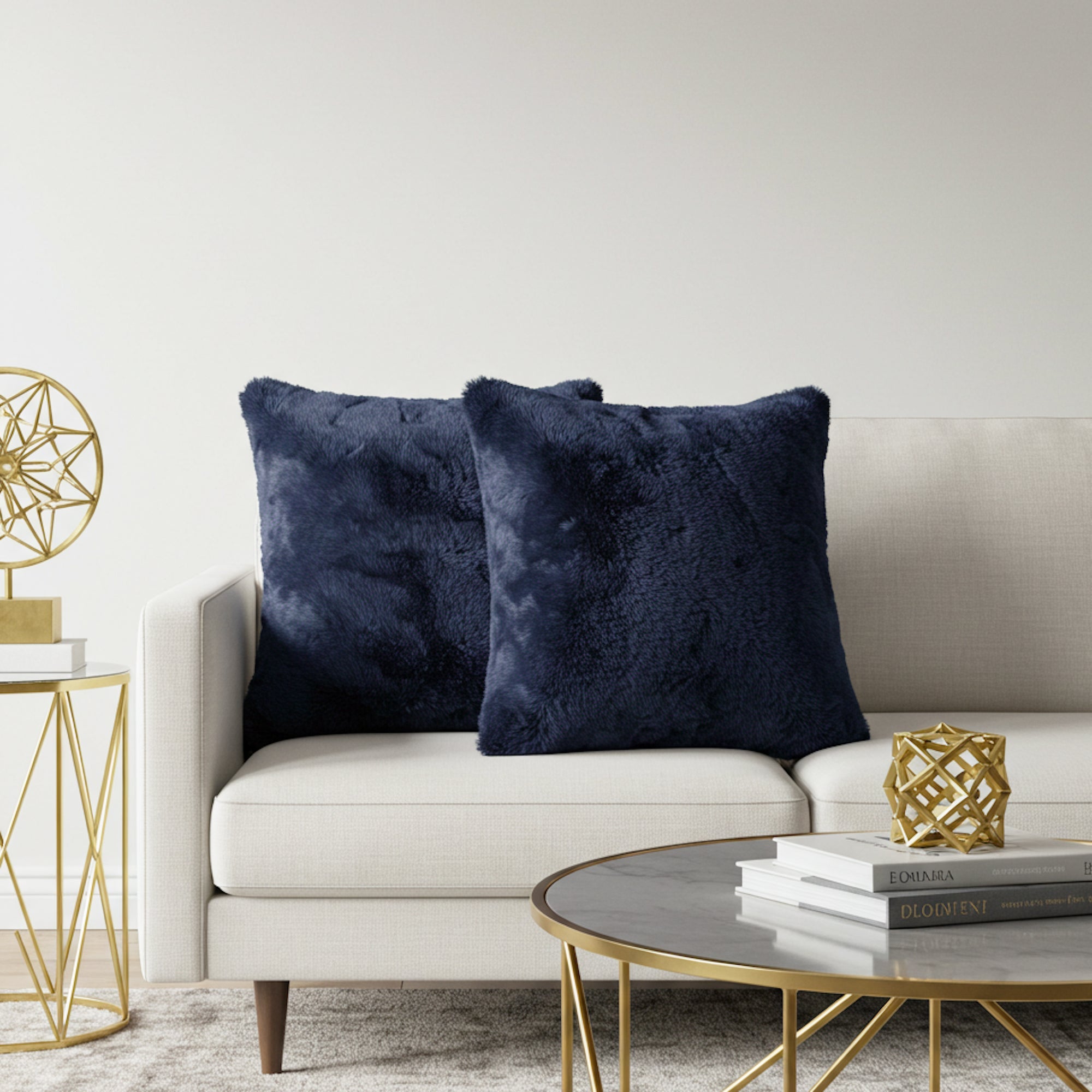 Two plush navy blue throw pillows displayed on a light beige sofa in a modern living room setting with gold accents.