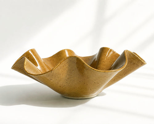 A sculptural ceramic bowl with a wavy, flared rim and glossy speckled tan-brown glaze