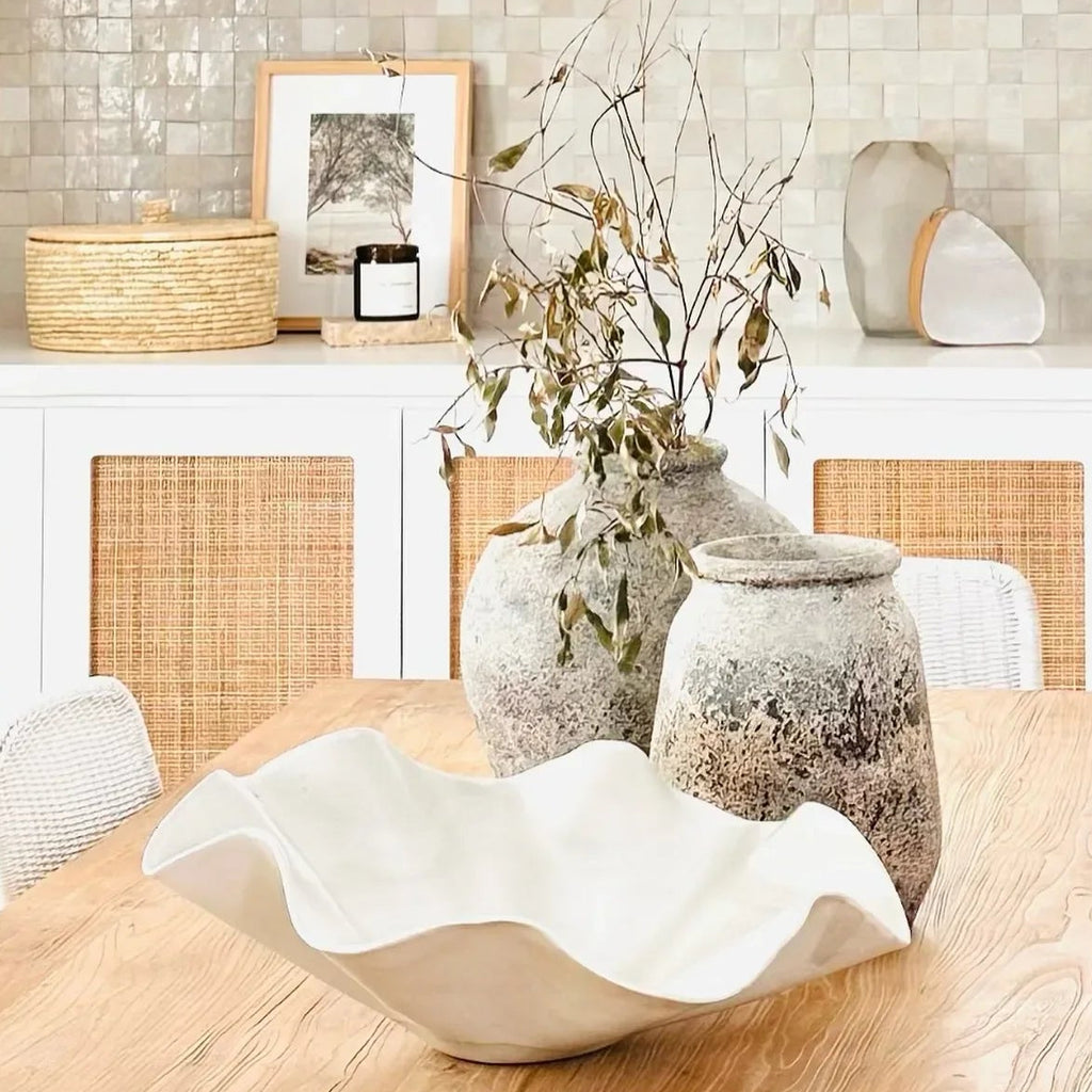 Dining room with wooden table, chairs, and oversized sculptural ceramic wave bowl.