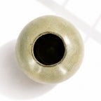 A round ceramic vase with a glossy, textured sage green glaze and a dark interior, photographed from a top-down angle.