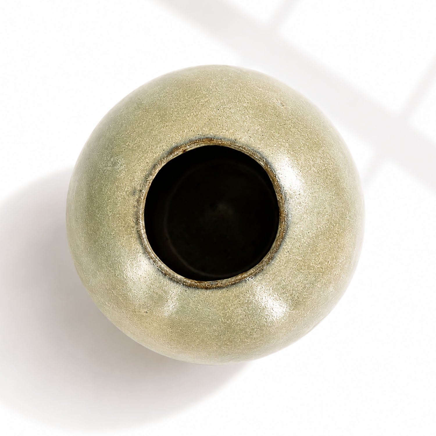 A round ceramic vase with a glossy, textured sage green glaze and a dark interior, photographed from a top-down angle.