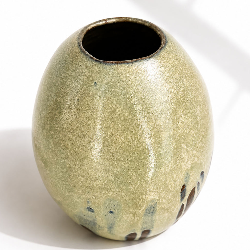 A large ceramic vase with a rounded, egg-shaped form, featuring a textured mint and beige glaze with dark brown and blue leaf-like accents near the base.