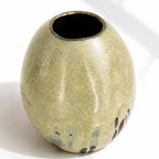 A large ceramic vase with a rounded, egg-shaped form, featuring a textured mint and beige glaze with dark brown and blue leaf-like accents near the base.