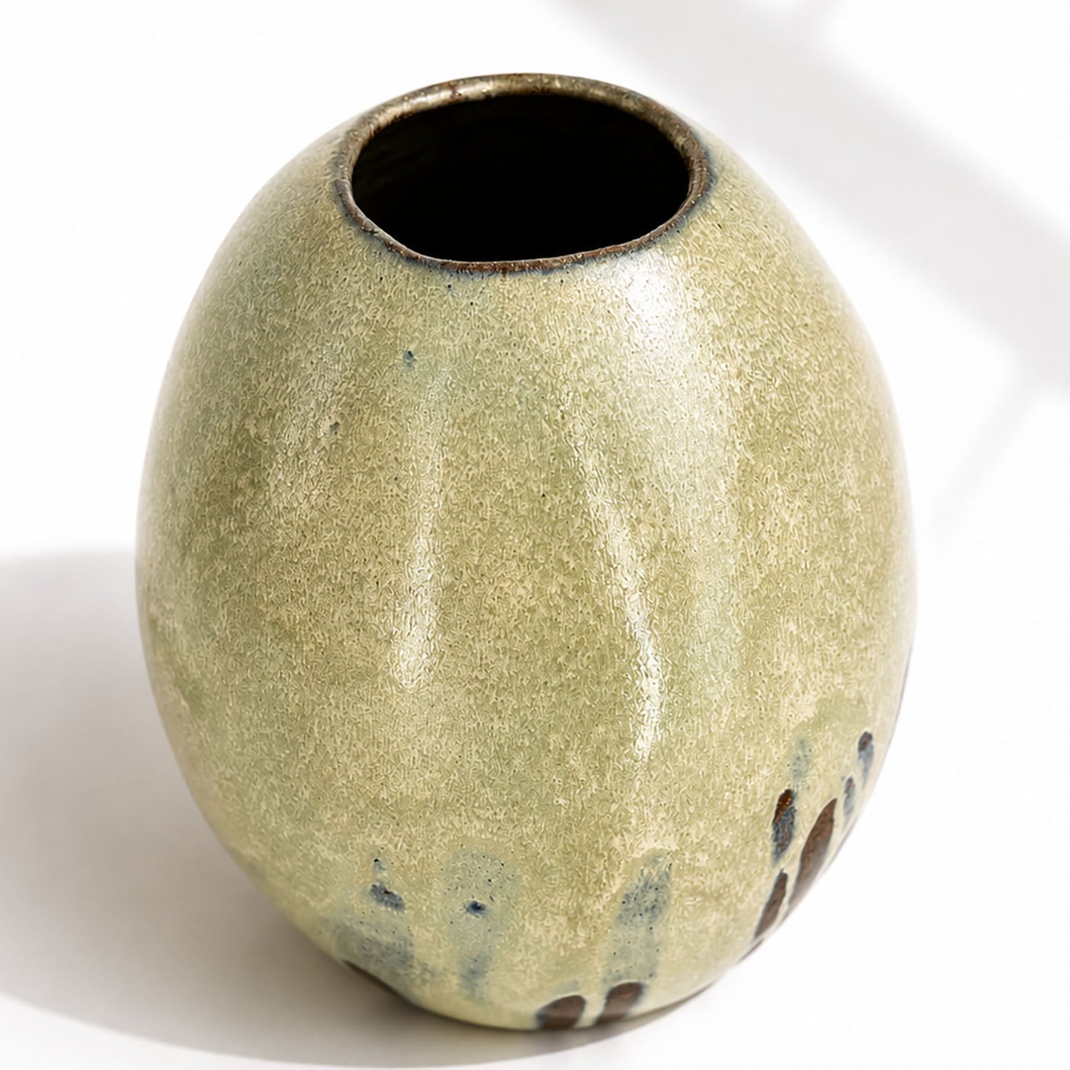 A large ceramic vase with a rounded, egg-shaped form, featuring a textured mint and beige glaze with dark brown and blue leaf-like accents near the base.