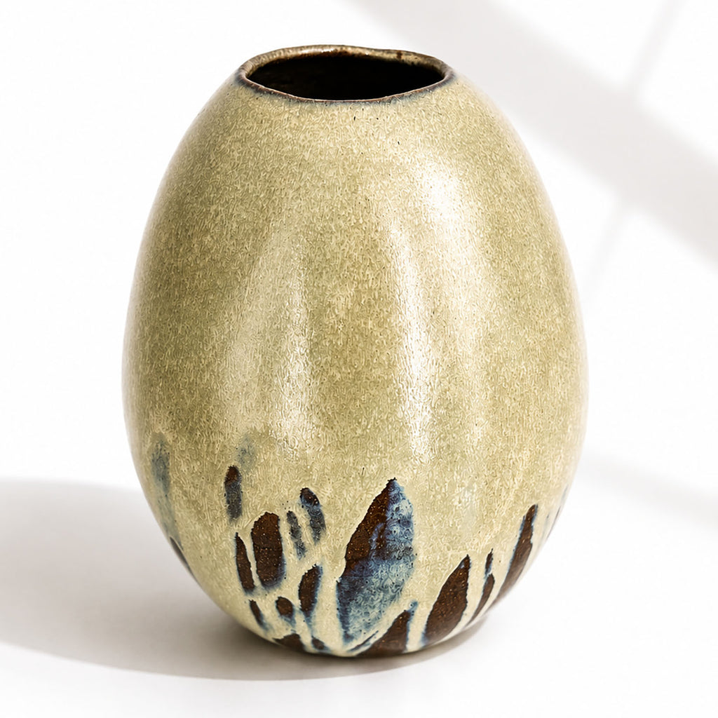 A large ceramic vase with a rounded, egg-shaped form, featuring a textured mint and beige glaze with dark brown and blue leaf-like accents near the base.