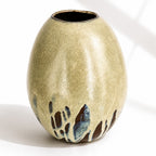A large ceramic vase with a rounded, egg-shaped form, featuring a textured mint and beige glaze with dark brown and blue leaf-like accents near the base.