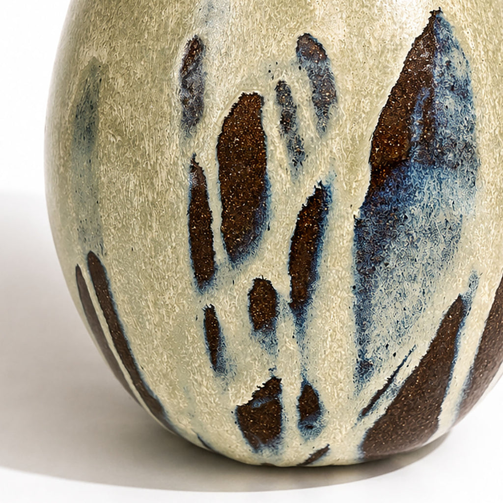 Close-up of a large ceramic vase with a textured, speckled glaze in cream, blue, and dark brown.