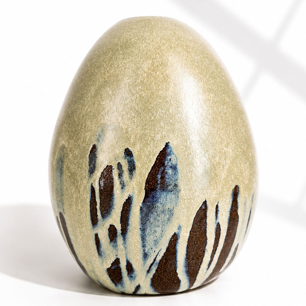 A large ceramic egg-shaped vase with a speckled mint glaze, decorated with dark brown and blue abstract leaf-like patterns near the base.