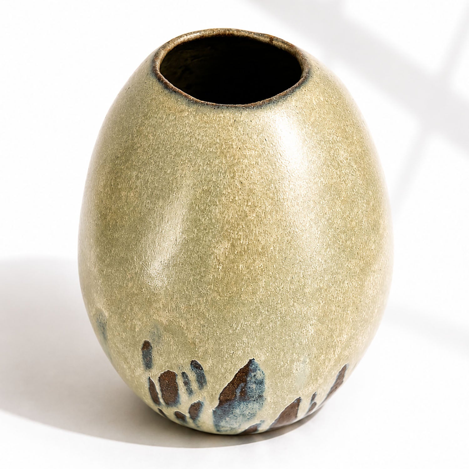 A large ceramic vase with a rounded, egg-shaped form, featuring a textured mint and beige glaze with dark brown and blue leaf-like accents near the base.