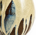 Close-up of a ceramic egg vase with a textured cream-beige glaze and irregular dark brown and blue abstract brushstroke patterns.