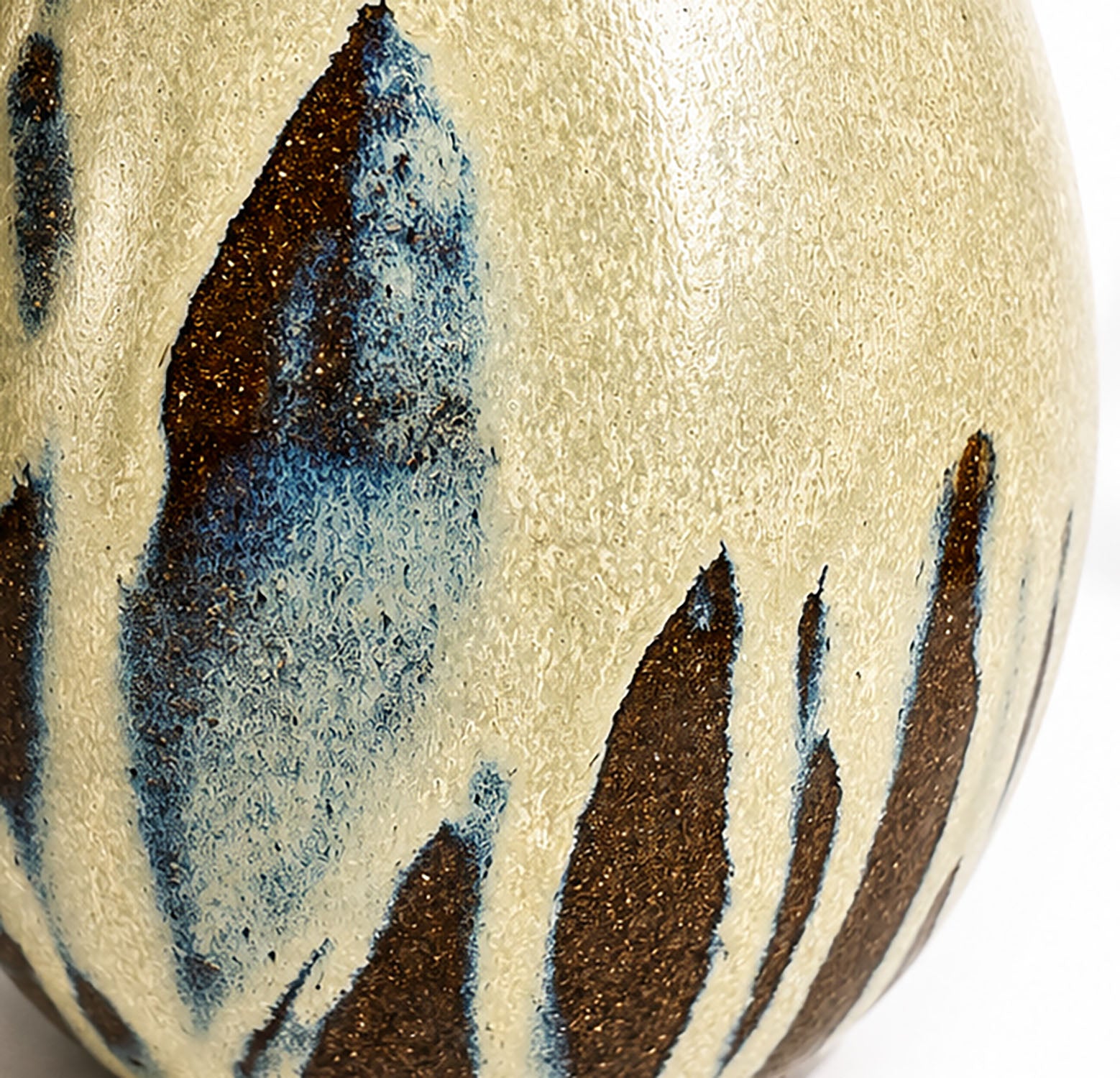 Close-up of a ceramic egg vase with a textured cream-beige glaze and irregular dark brown and blue abstract brushstroke patterns.