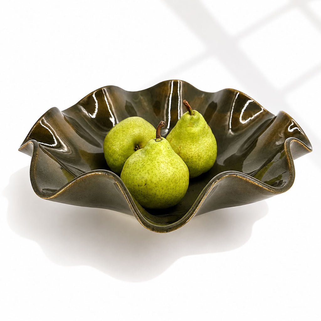 An oily Rockpool coloured wavy ceramic bowl with a glossy glaze, containing three green pears, set against a clean white background with soft window shadow patterns.
