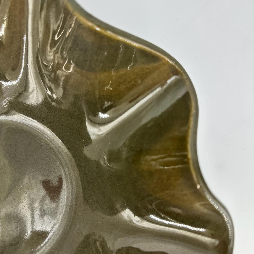 Close-up of a glossy ceramic waved bowl with a scalloped edge and a circular recess, showing a brown and olive glaze on a white background.