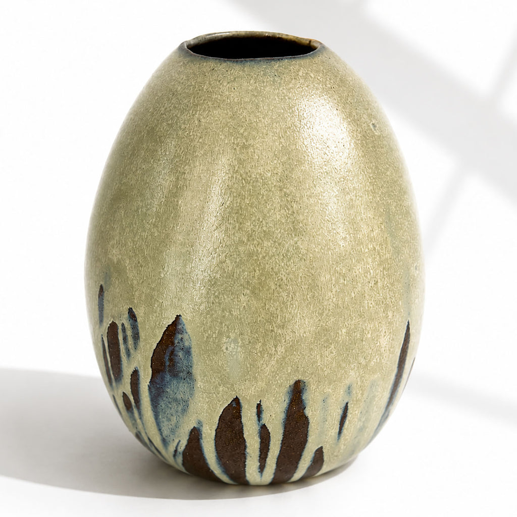 A large ceramic vase with a rounded, egg-shaped form, featuring a textured mint and beige glaze with dark brown and blue leaf-like accents near the base.