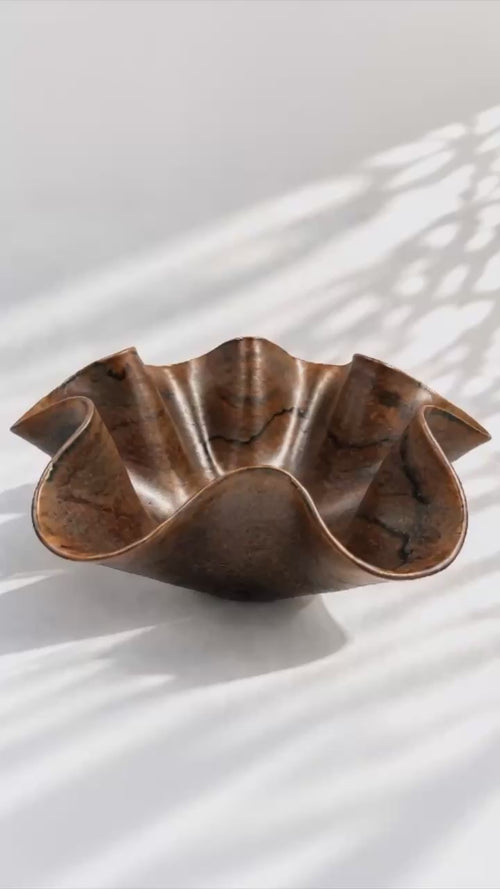 360 video of a sculptural chocolate glaze bowl with a wavy, fluted rim and a satin finish, showing warm bronze-brown tones with darker oxidized highlights.