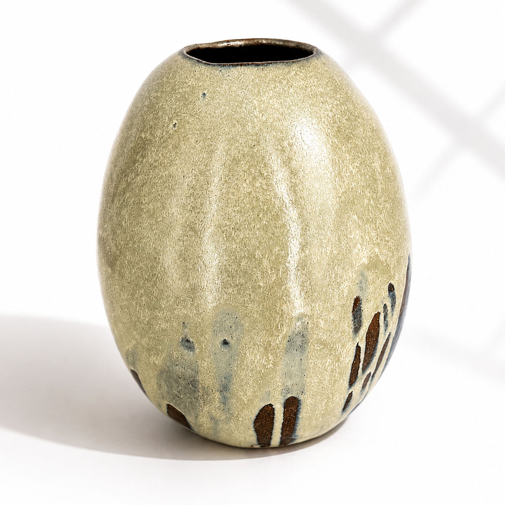 A large ceramic vase with a rounded, egg-shaped form, featuring a textured mint and beige glaze with dark brown and blue leaf-like accents near the base.